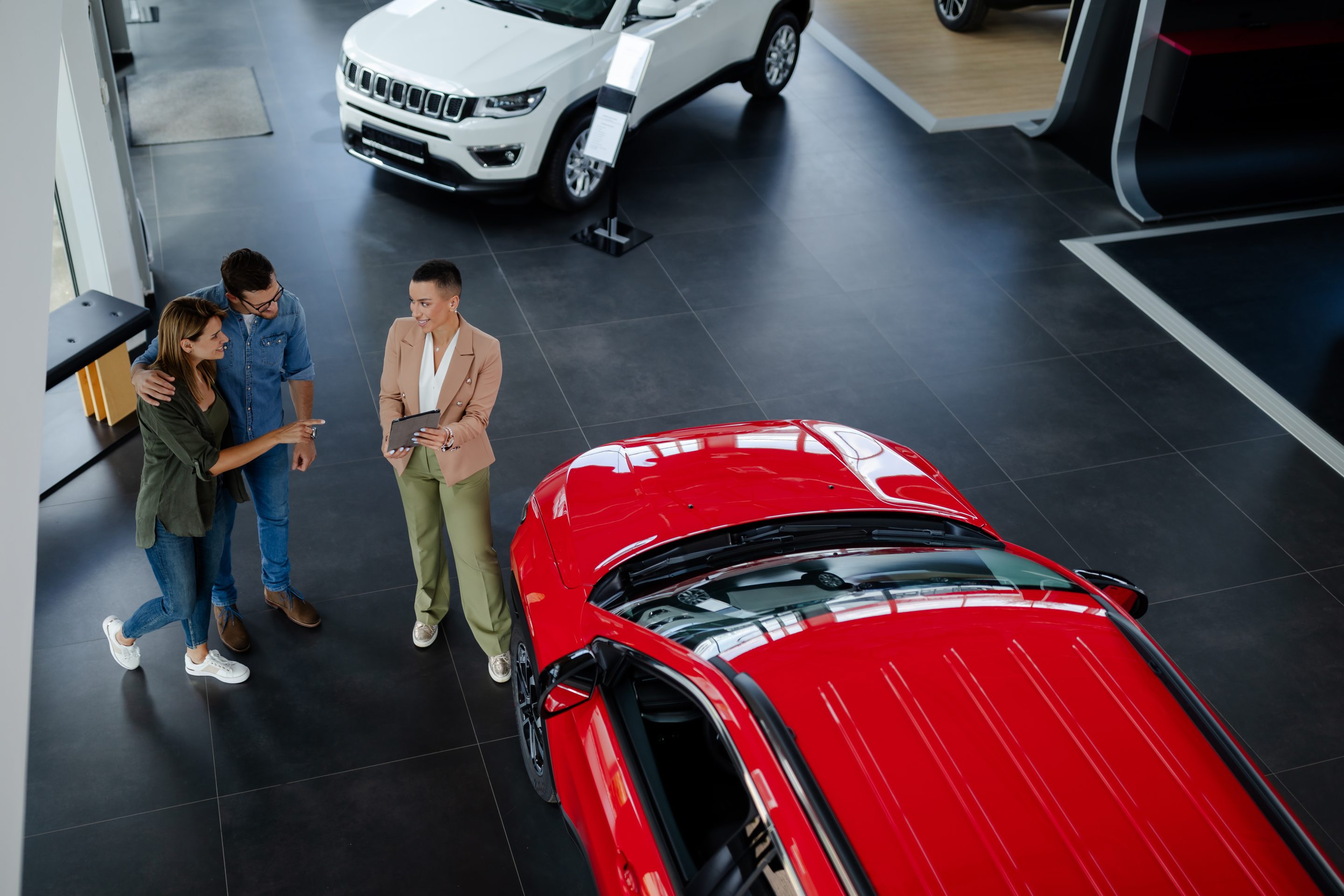 young professional saleswoman demonstrating document to customers buying new car in dealership.
