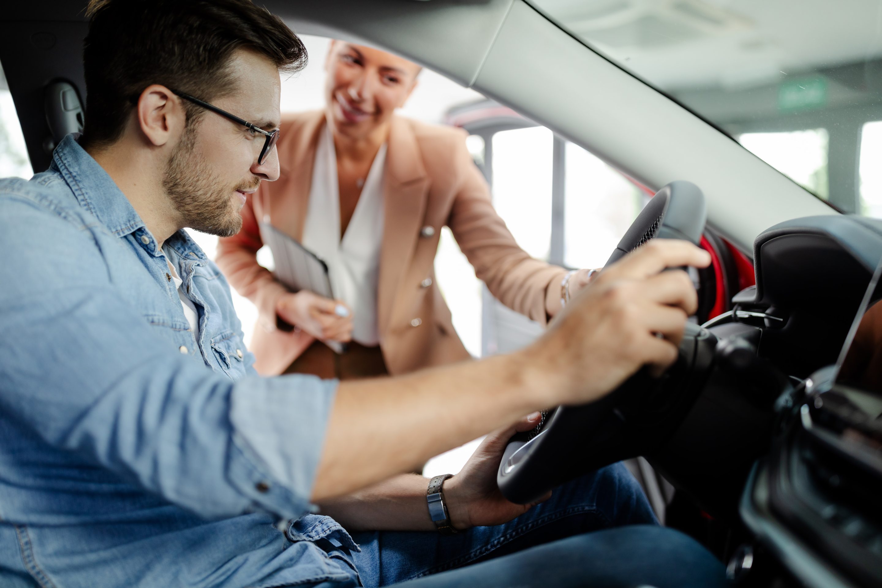 Saleswoman is showing new car to young Caucasian man in showroom.